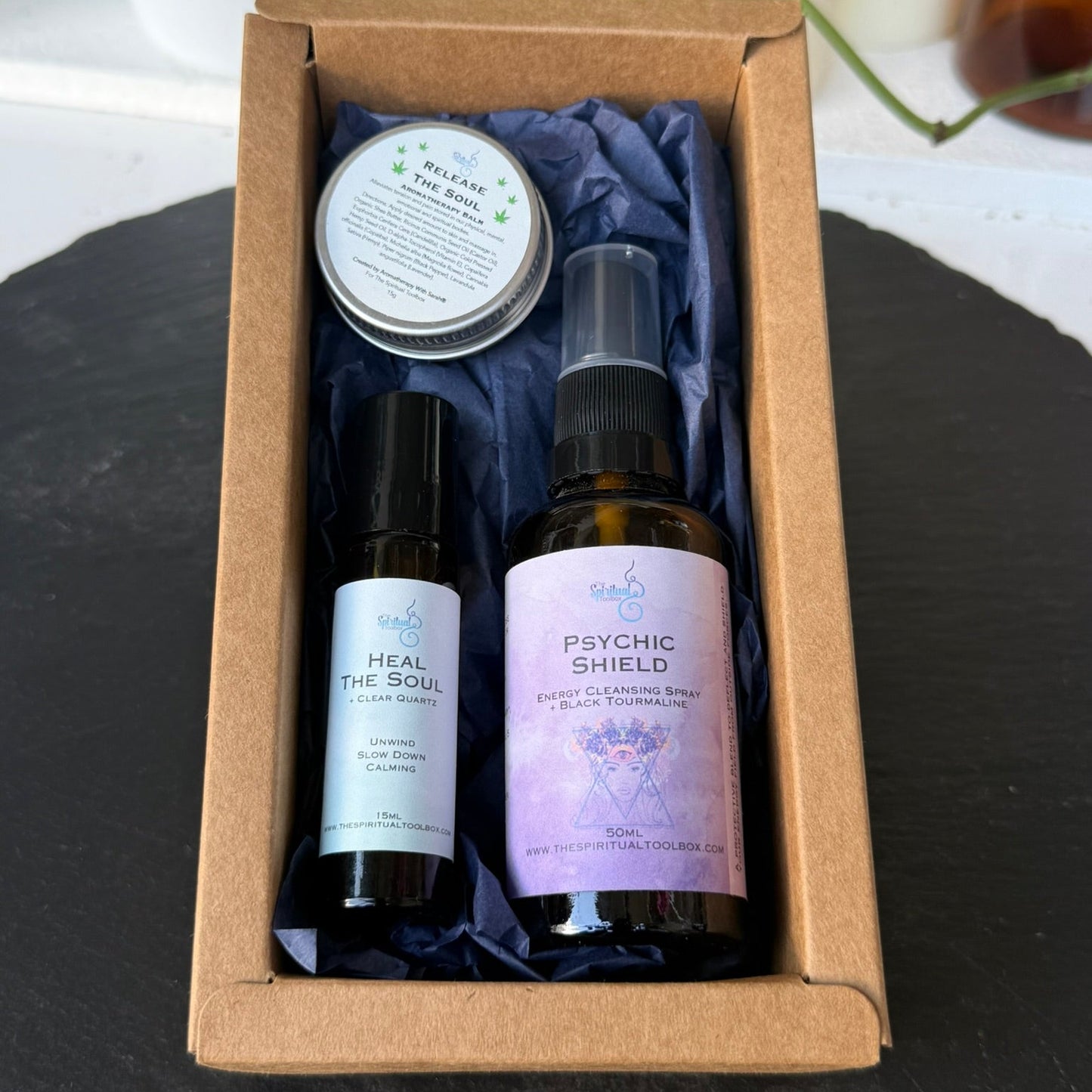 Set of natural products including bottles and a tin in a cardboard box on a dark surface.