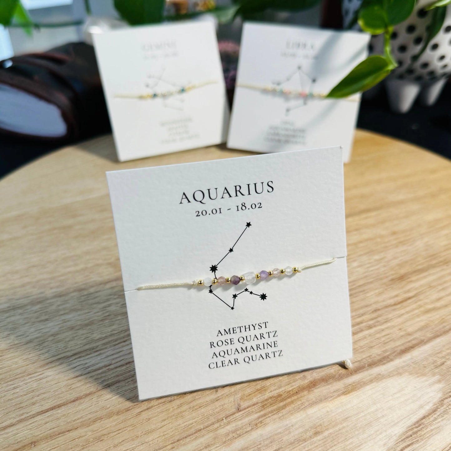 Aquarius-themed bracelet on a display card with a wooden surface background