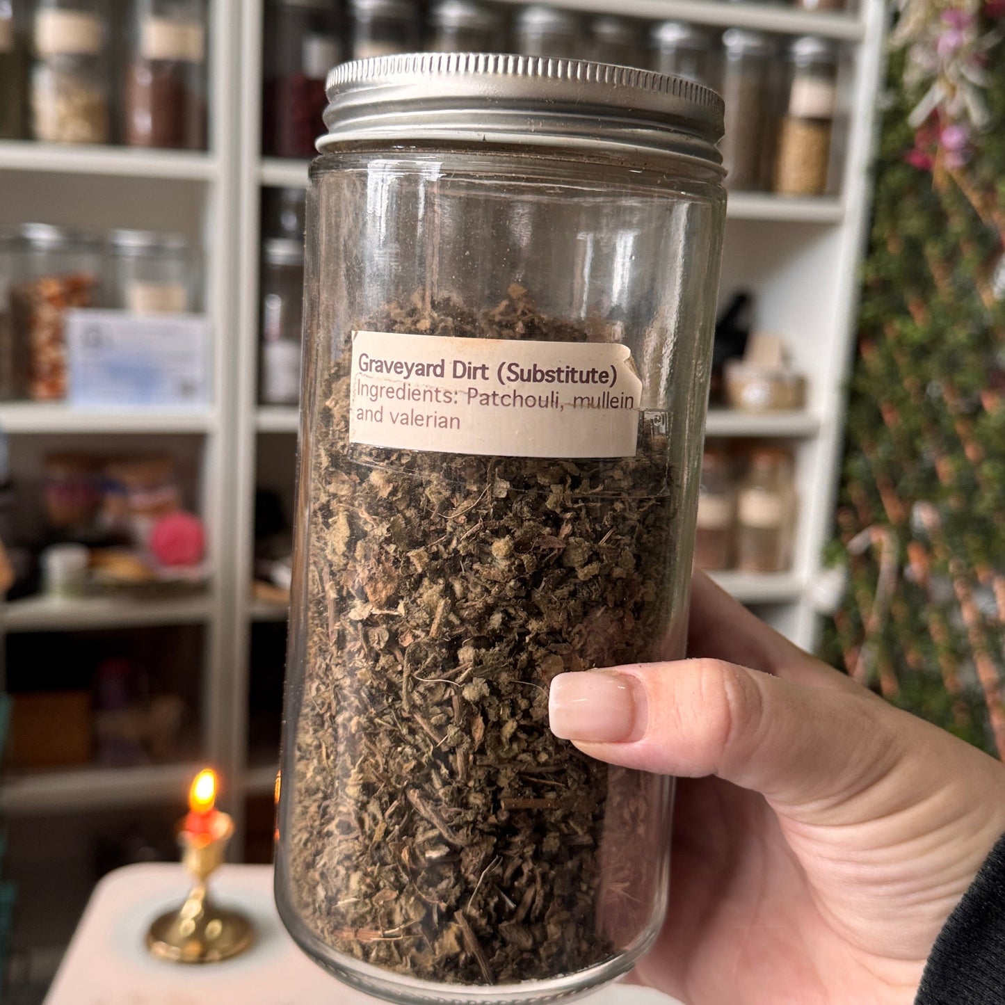 Hand holding a jar of dried herbs with a apothecary the background