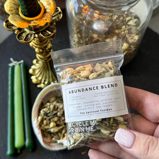 Hand holding a package labeled 'Abundance Blend' with candles and jars in the background.