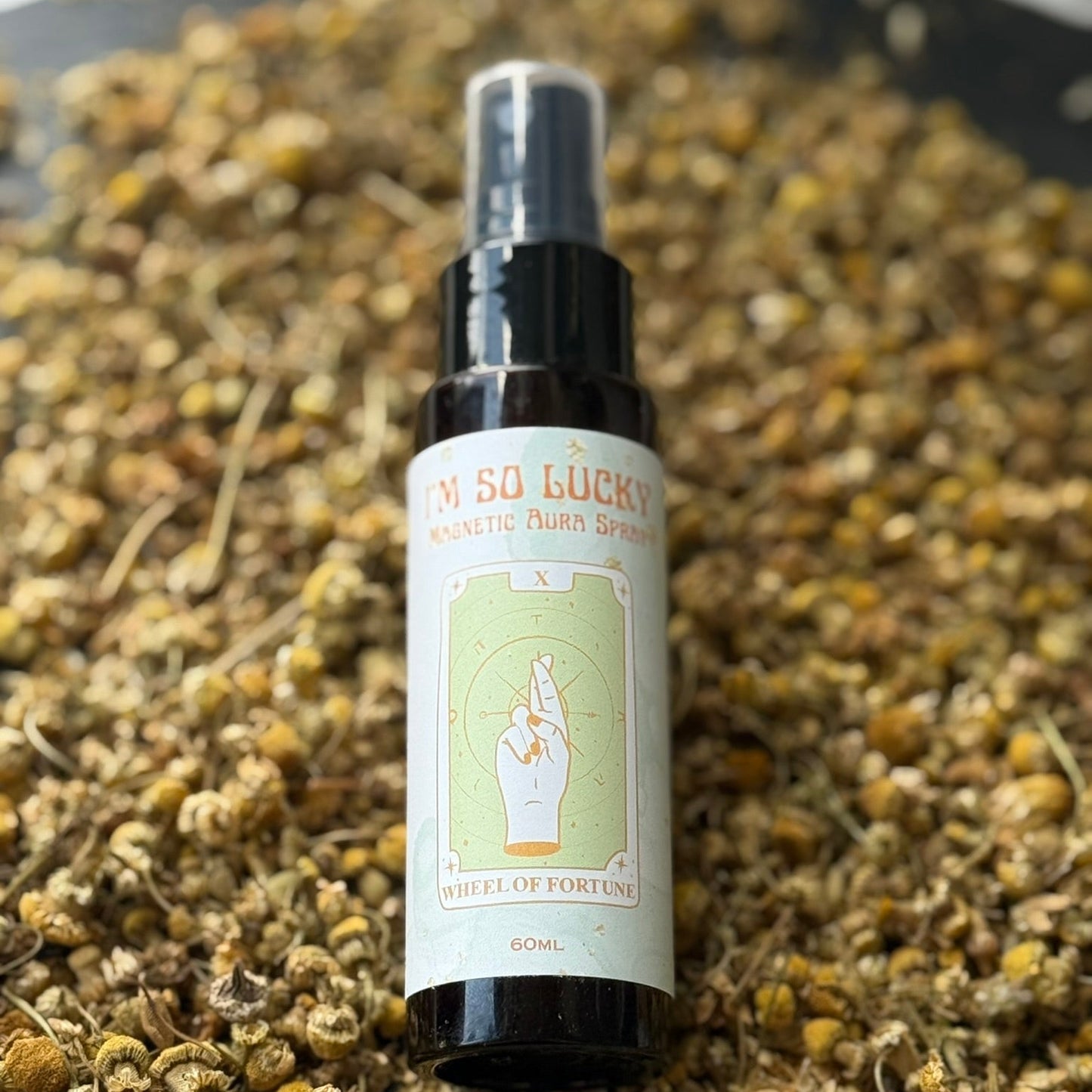 Spray bottle labeled 'I'M So Lucky' on a bed of dried herbs