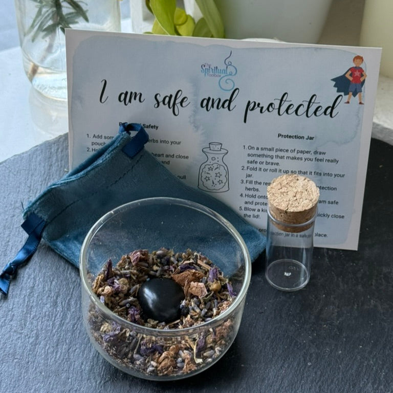 Protection jar with herbs and a black stone, accompanied by a card and blue fabric on a gray surface.