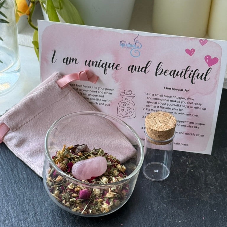 Glass jar with dried herbs and a pink stone, pink pouch, and instruction card on a dark surface.