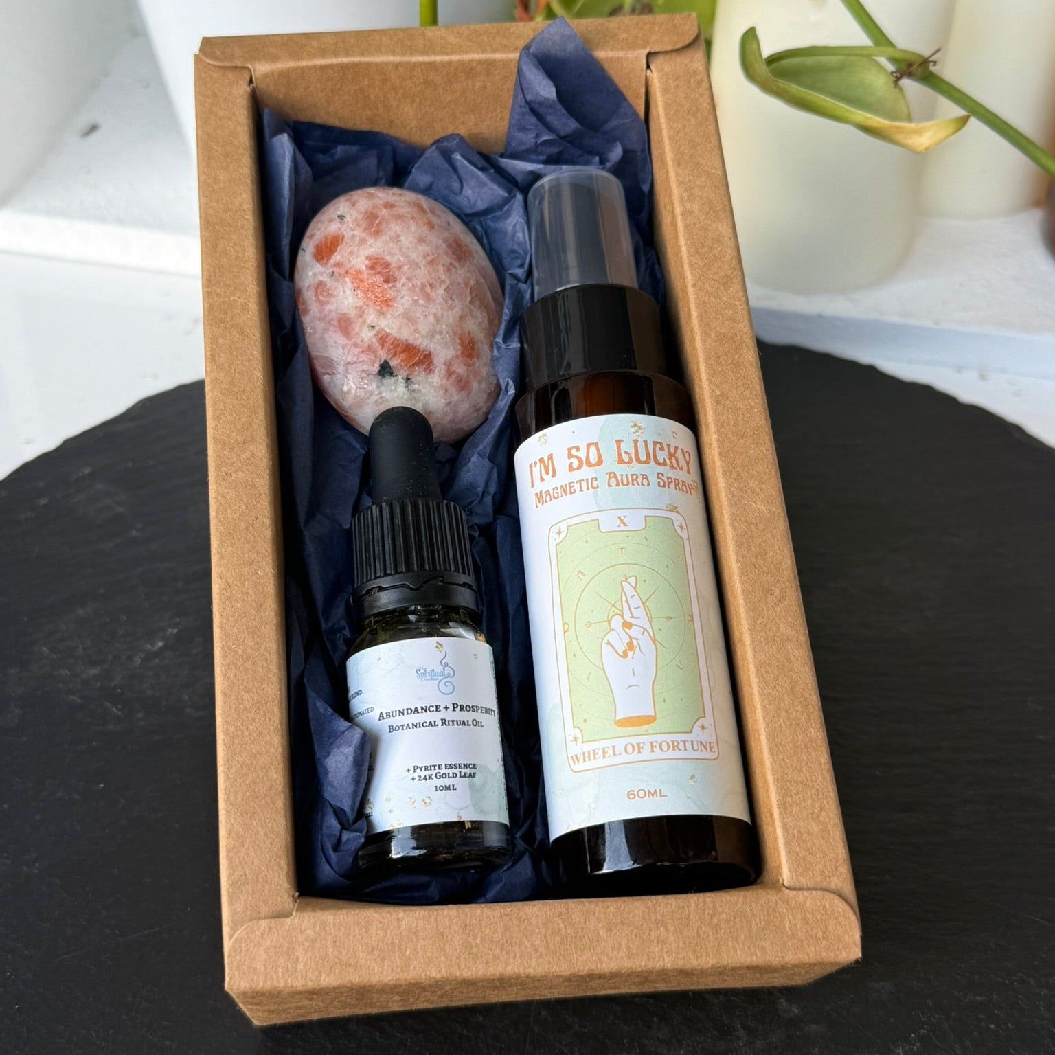 Set of wellness products including a bottle, vial, and stone in a brown box with a plant and candle in the background.