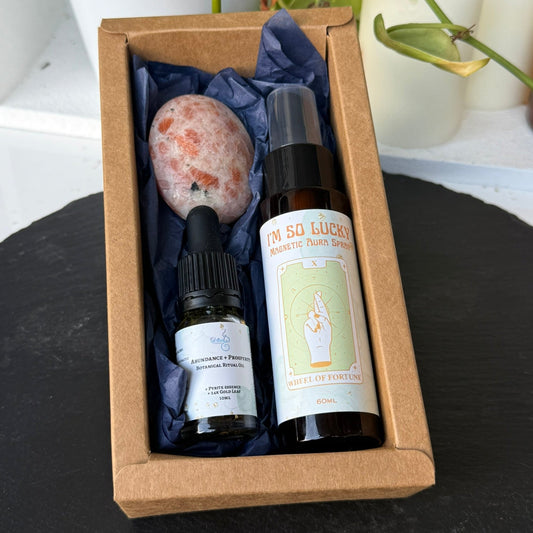 Set of wellness products including a bottle, vial, and stone in a brown box with a plant and candle in the background.
