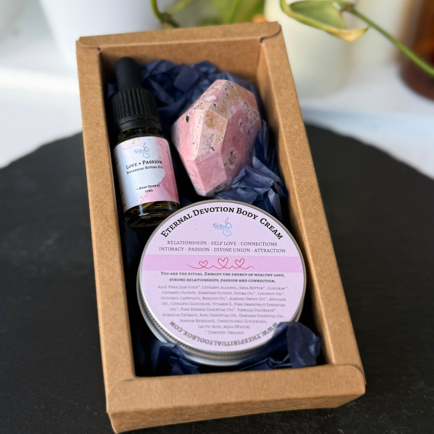 Set of beauty products including a bottle, cream, and stone in a brown box on a black surface.