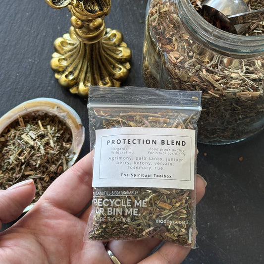 Hand holding a package of 'Protection Blend' with a lit candle and jars in the background.