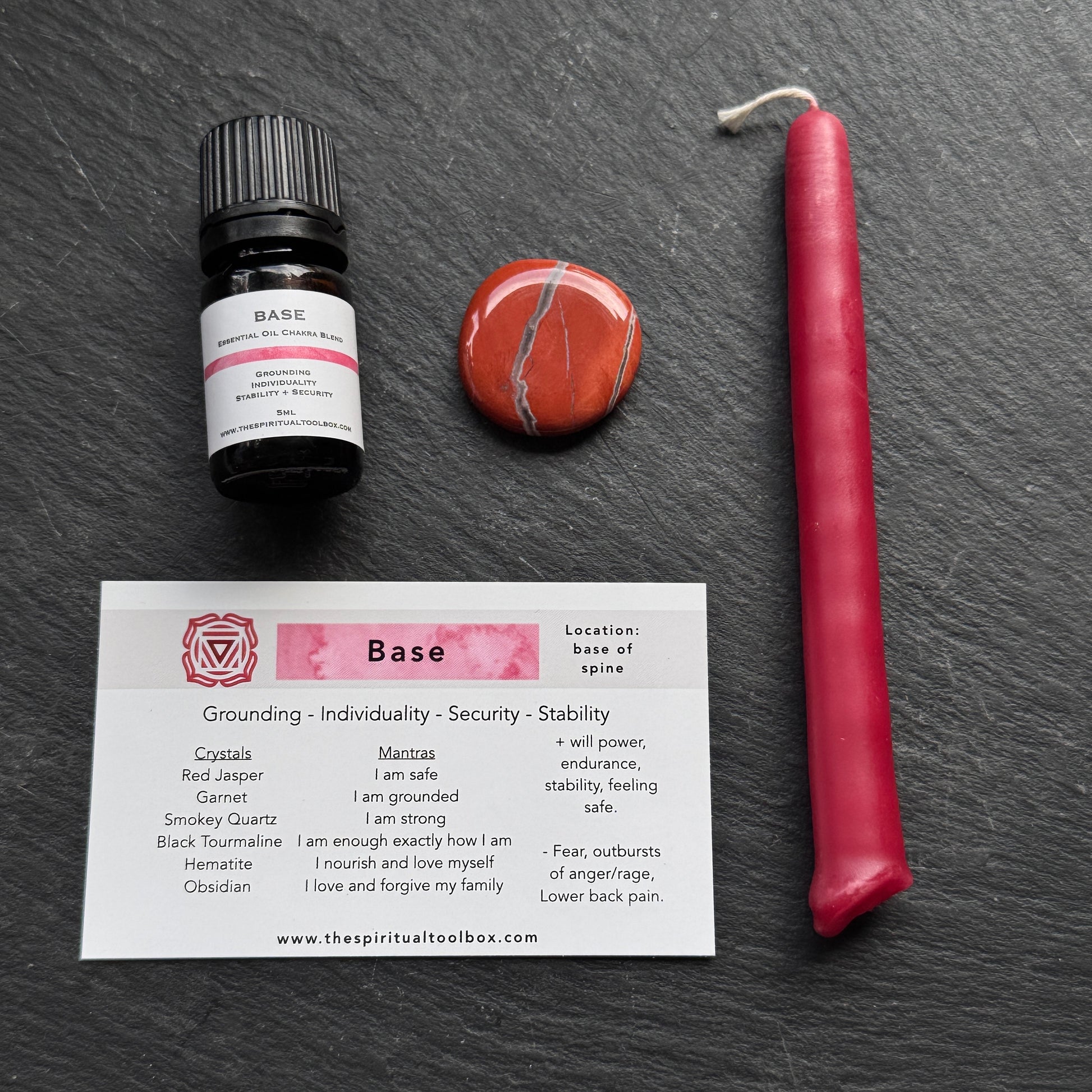 Base essential oil bottle, red candle, red Jasper stone, and a card with base information on a dark surface