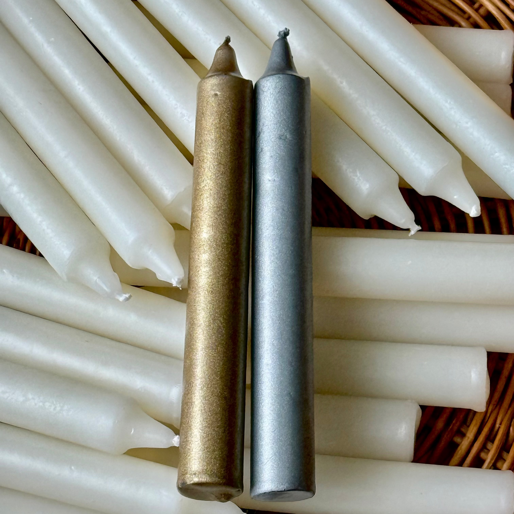 Two candles objects, one gold and one silver, on a textured black surface.