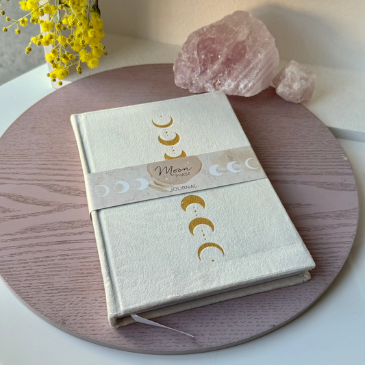 Notebook with moon phases design on a wooden surface with flowers and crystals.