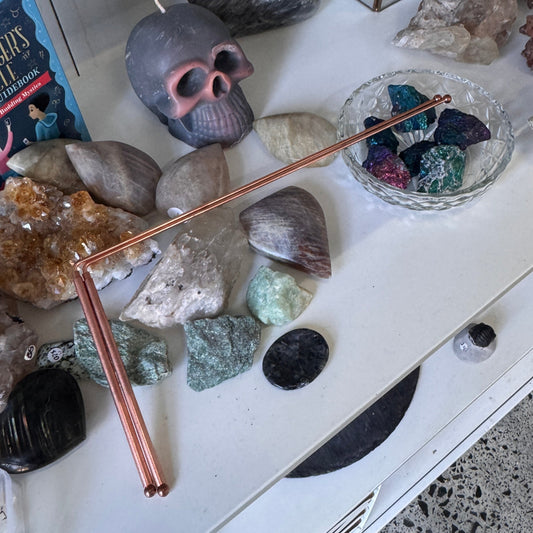 A tabletop display featuring a skull-shaped candle with a white wick, surrounded by various polished stones, crystals, and a copper-colored rod on a white surface.