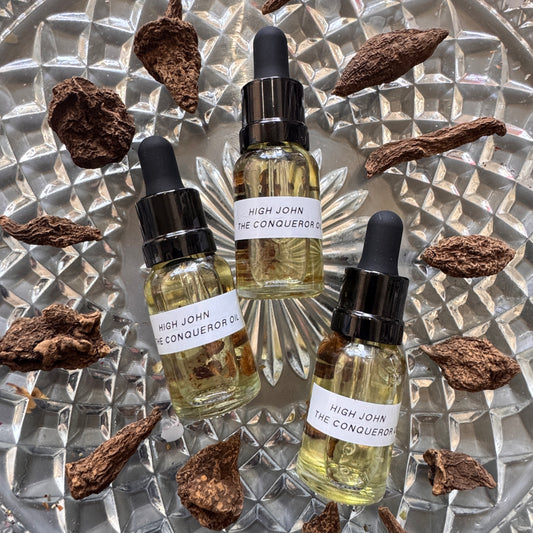 Three bottles of 'High John the Conqueror' oil with droppers on a textured metallic surface.