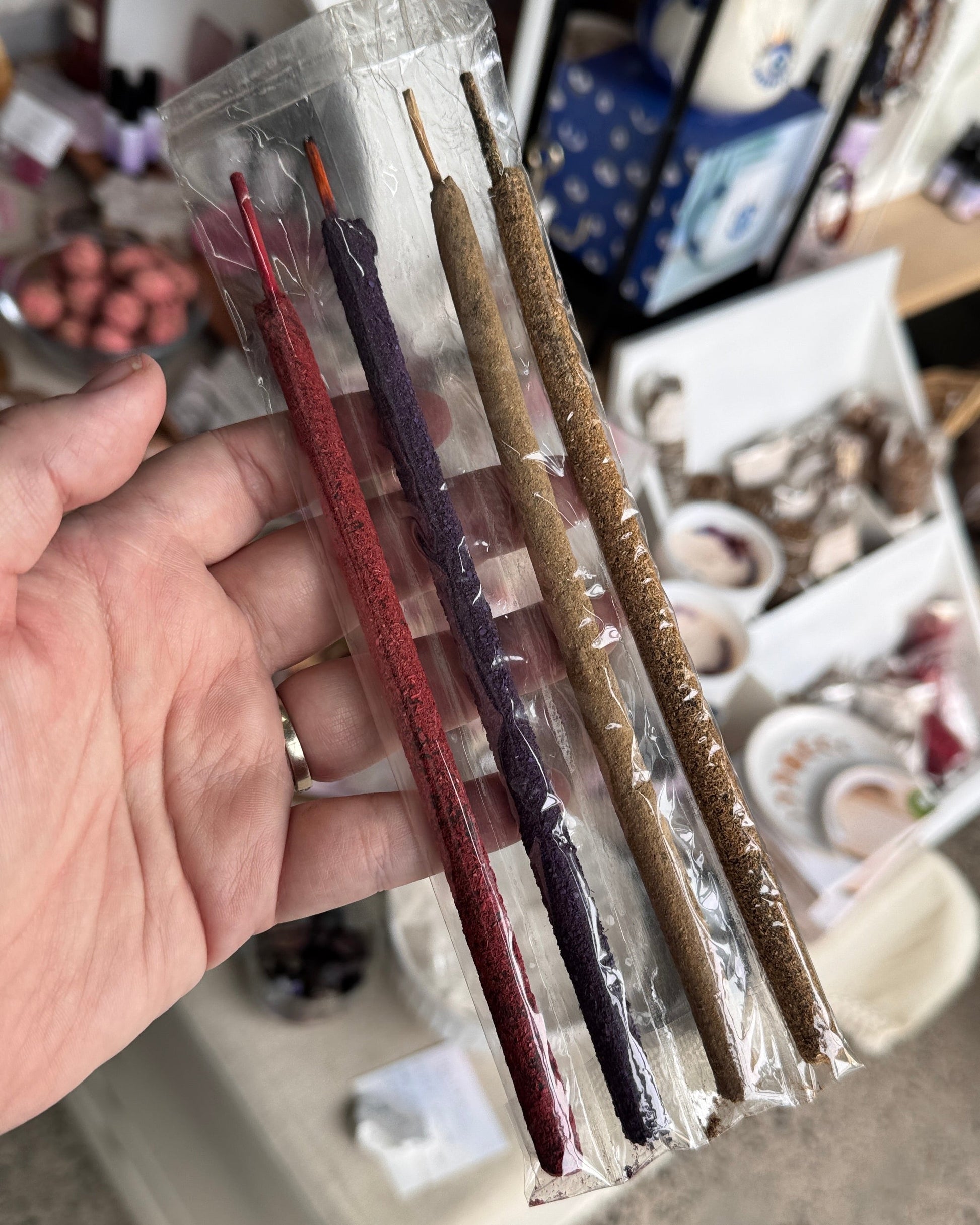Three incense sticks in clear packaging held by a hand with a blurred background